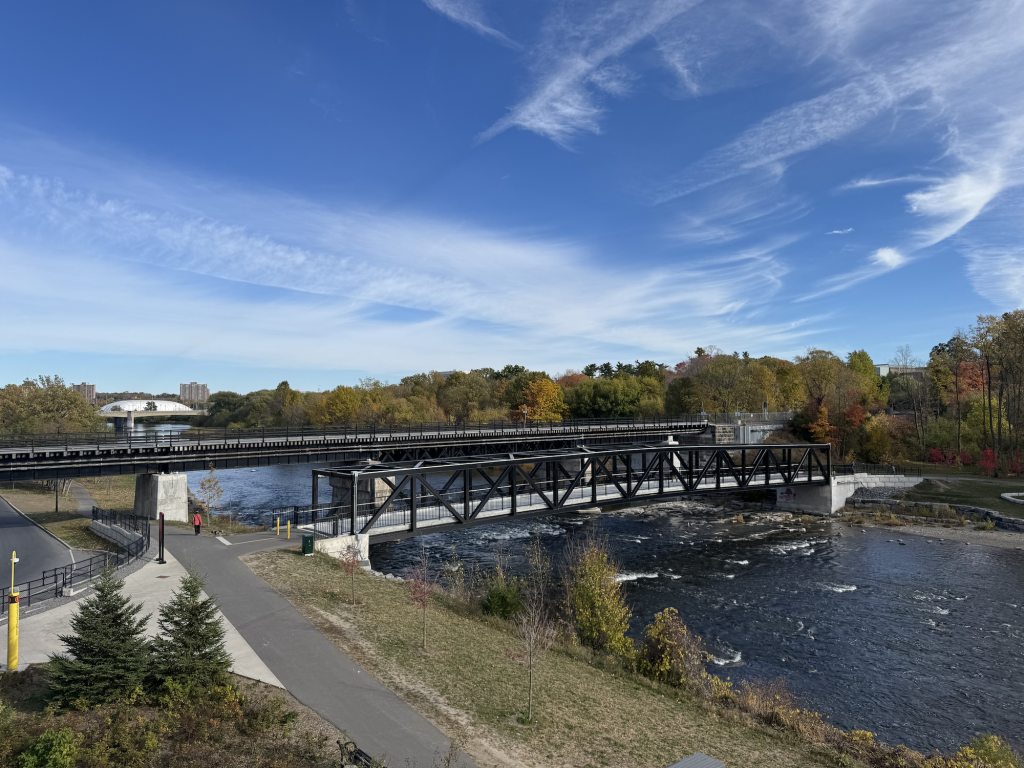 View of the rail and pedestrian bridges over the water.  A multi-use pathway in the foreground.