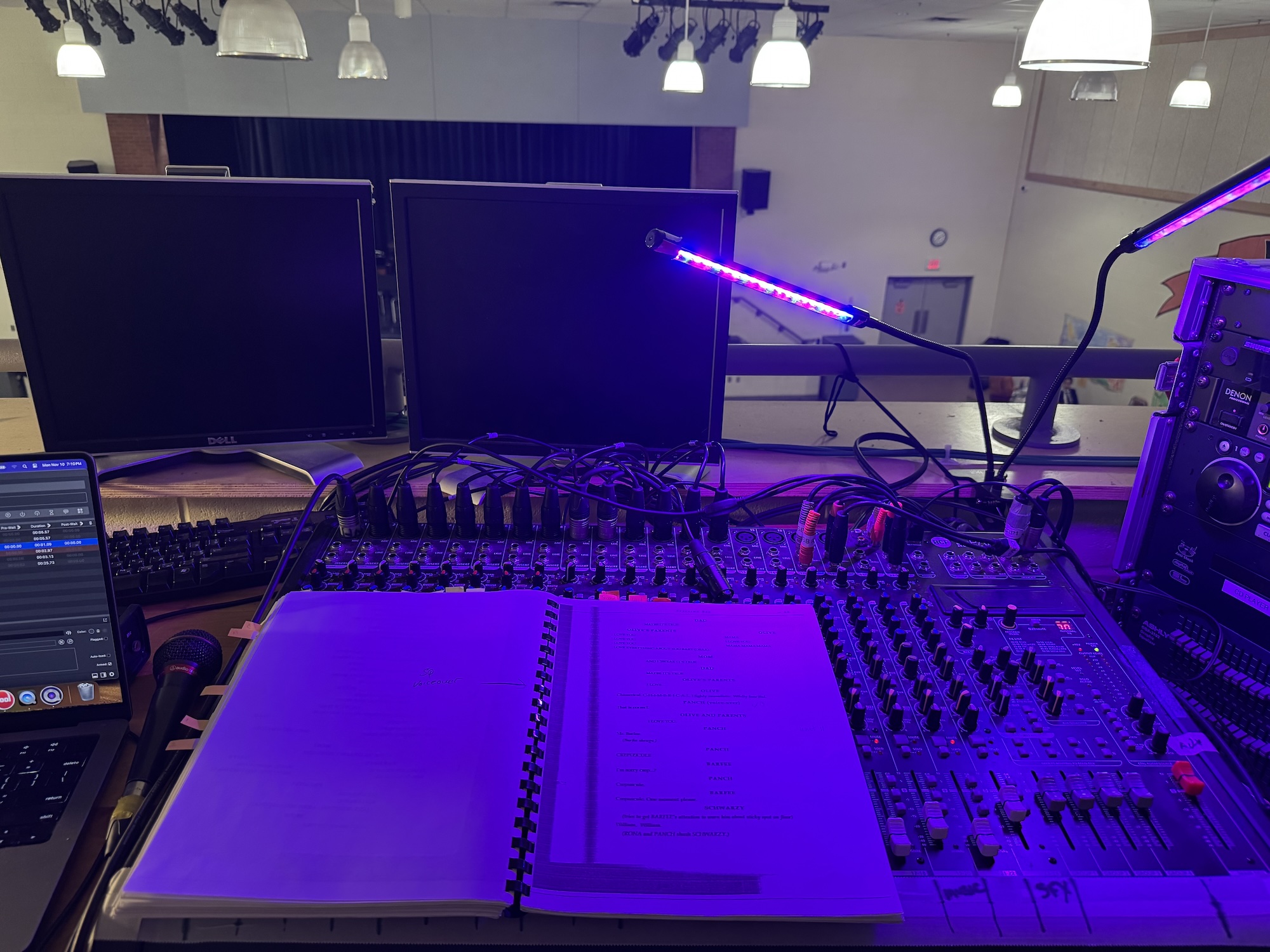 A script sitting atop an audio mixing console. A stage is visible in the background.
